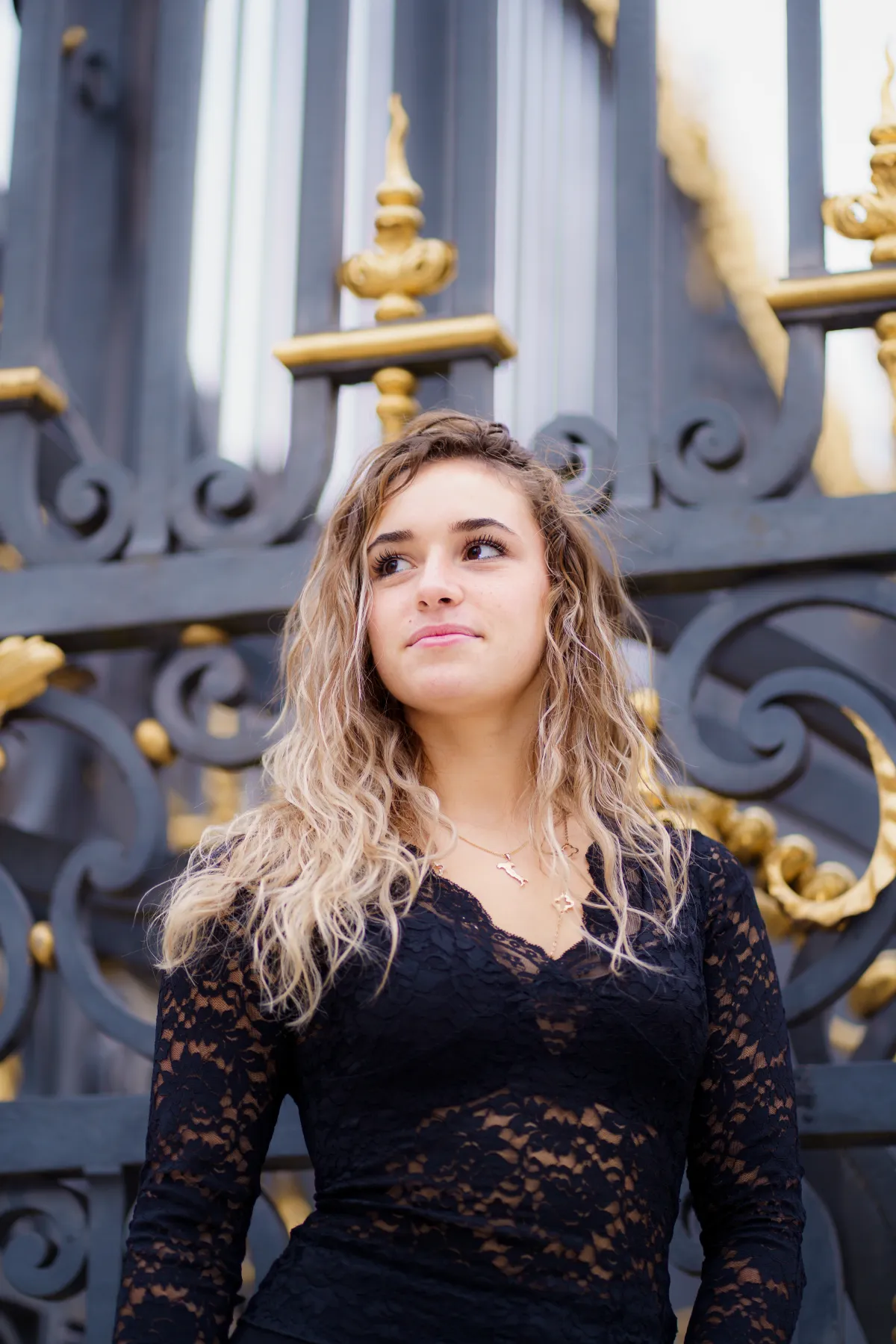 Femme en dentelle noire devant une grille dorée